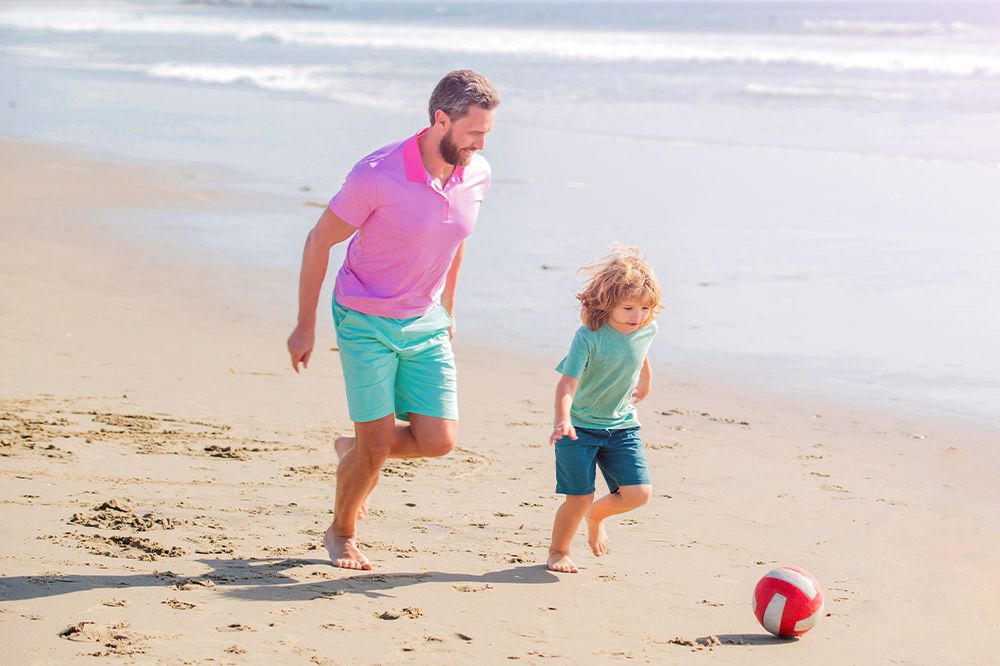 single father and child at the beach playing soccer